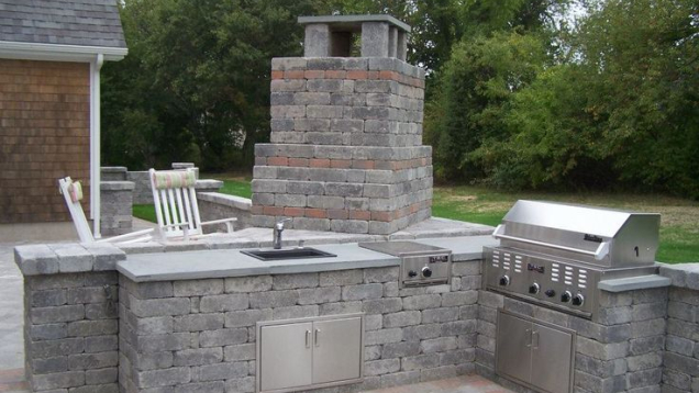 Outdoor kitchen with sink and grill on paver patio.